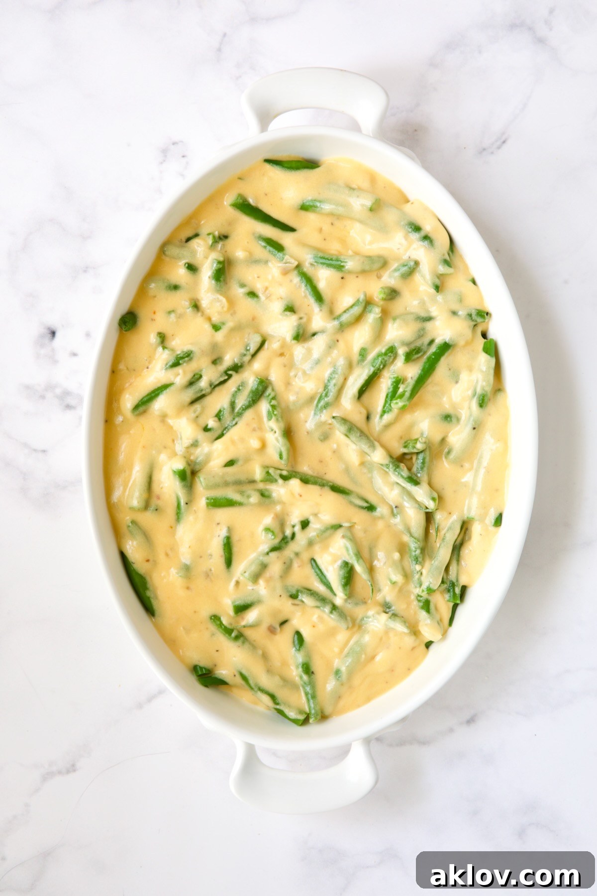 Irresistible Cheesy Green Bean Bake 11 Green beans in a gratin dish generously covered with creamy cheese sauce, ready for the topping.