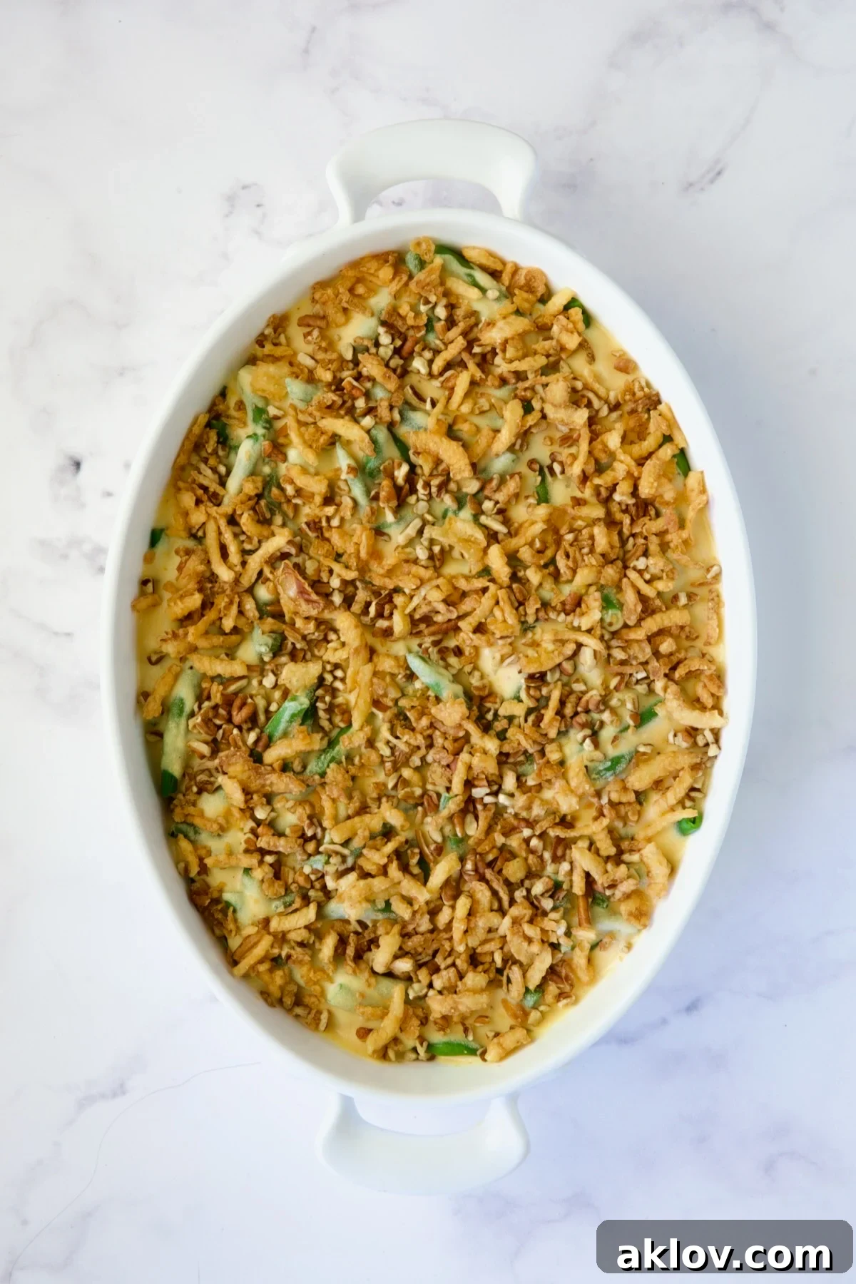 Fully assembled unbaked green bean casserole, topped with a generous layer of chopped pecans and crispy fried onions, ready for the oven.