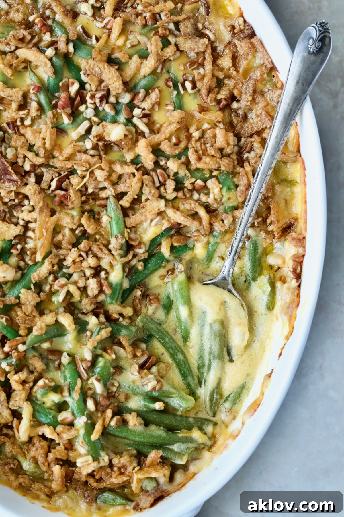 Irresistible Cheesy Green Bean Bake 14 Cheesy Green Bean Casserole in a white oval gratin dish with a serving spoon, highlighting the golden topping.