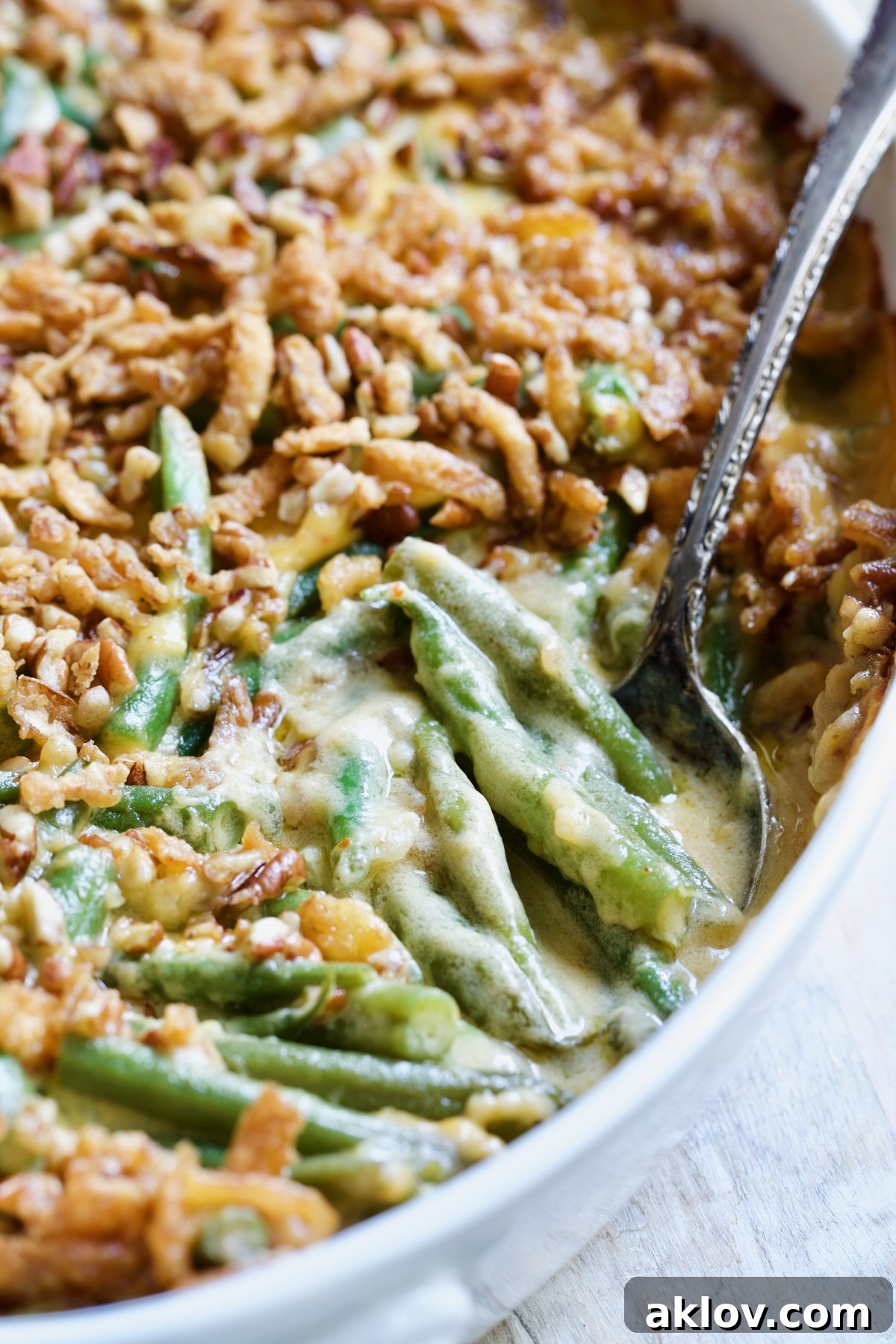 Irresistible Cheesy Green Bean Bake 15 Cheesy Green Bean Casserole with a golden pecan and crispy onion topping, served with a spoon.