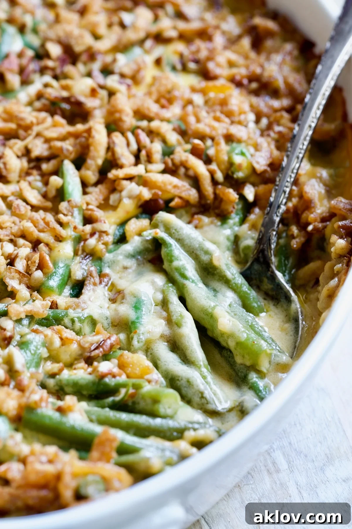 A delectable Cheesy Green Bean Casserole, adorned with a perfectly golden-brown pecan and crispy fried onion topping, served with a silver spoon ready for digging in.