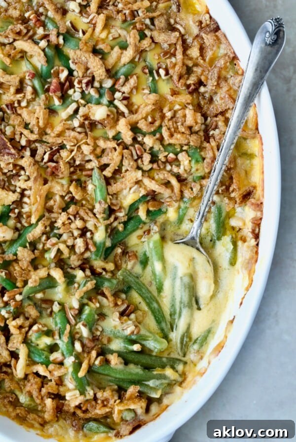 Cheesy Green Bean Casserole in white oval gratin dish with serving spoon.