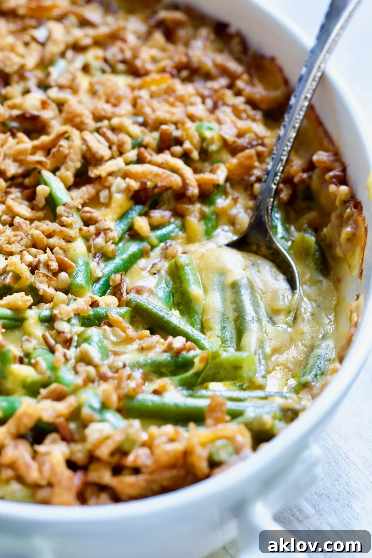 Close-up of Cheesy Green Bean Casserole in a white oval gratin dish, showing a portion scooped out to reveal the tender green beans drenched in creamy cheese sauce.