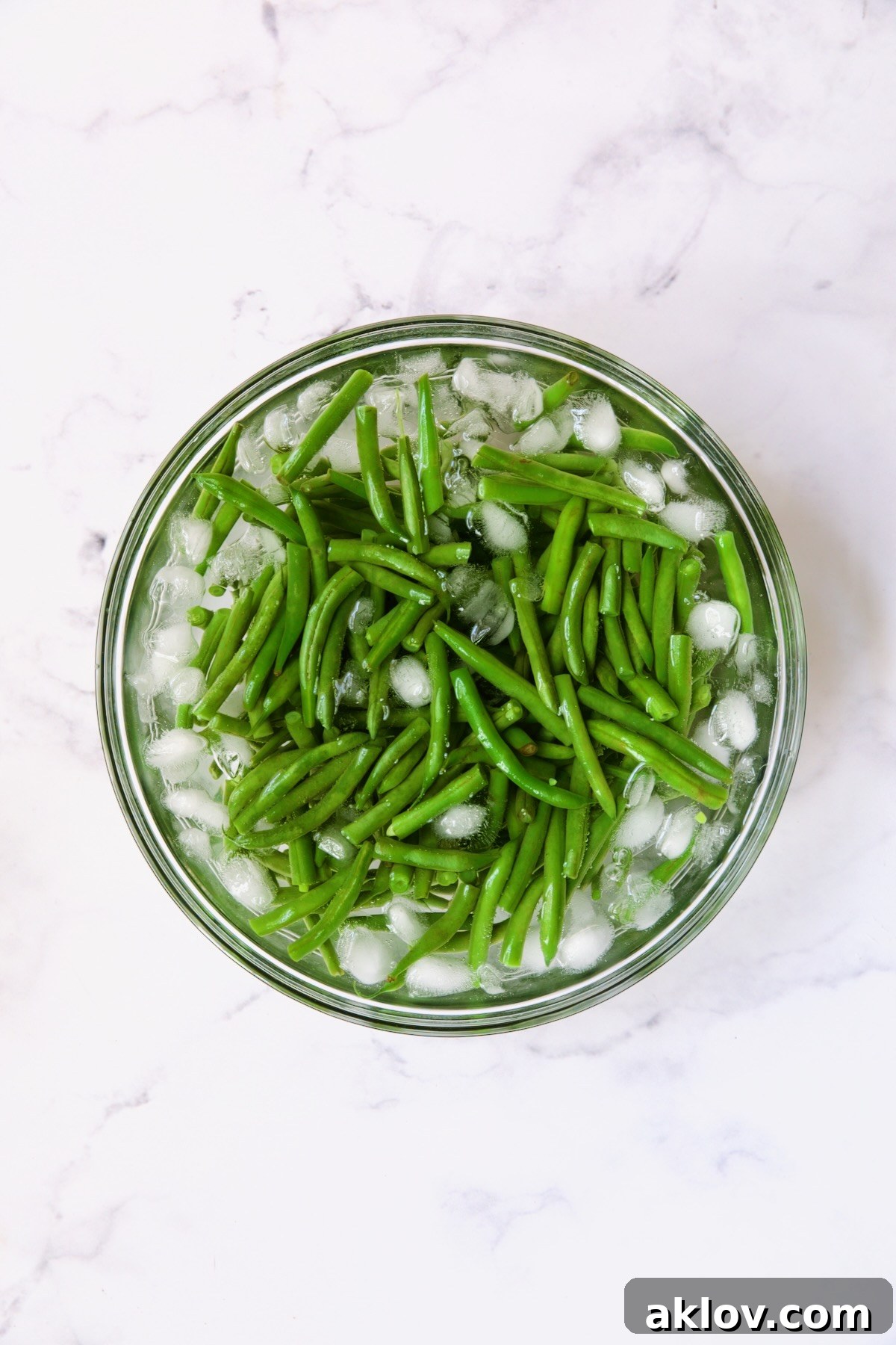 Irresistible Cheesy Green Bean Bake 5 Blanched green beans submerged in an ice bath in a clear glass bowl, showcasing their vibrant green color.