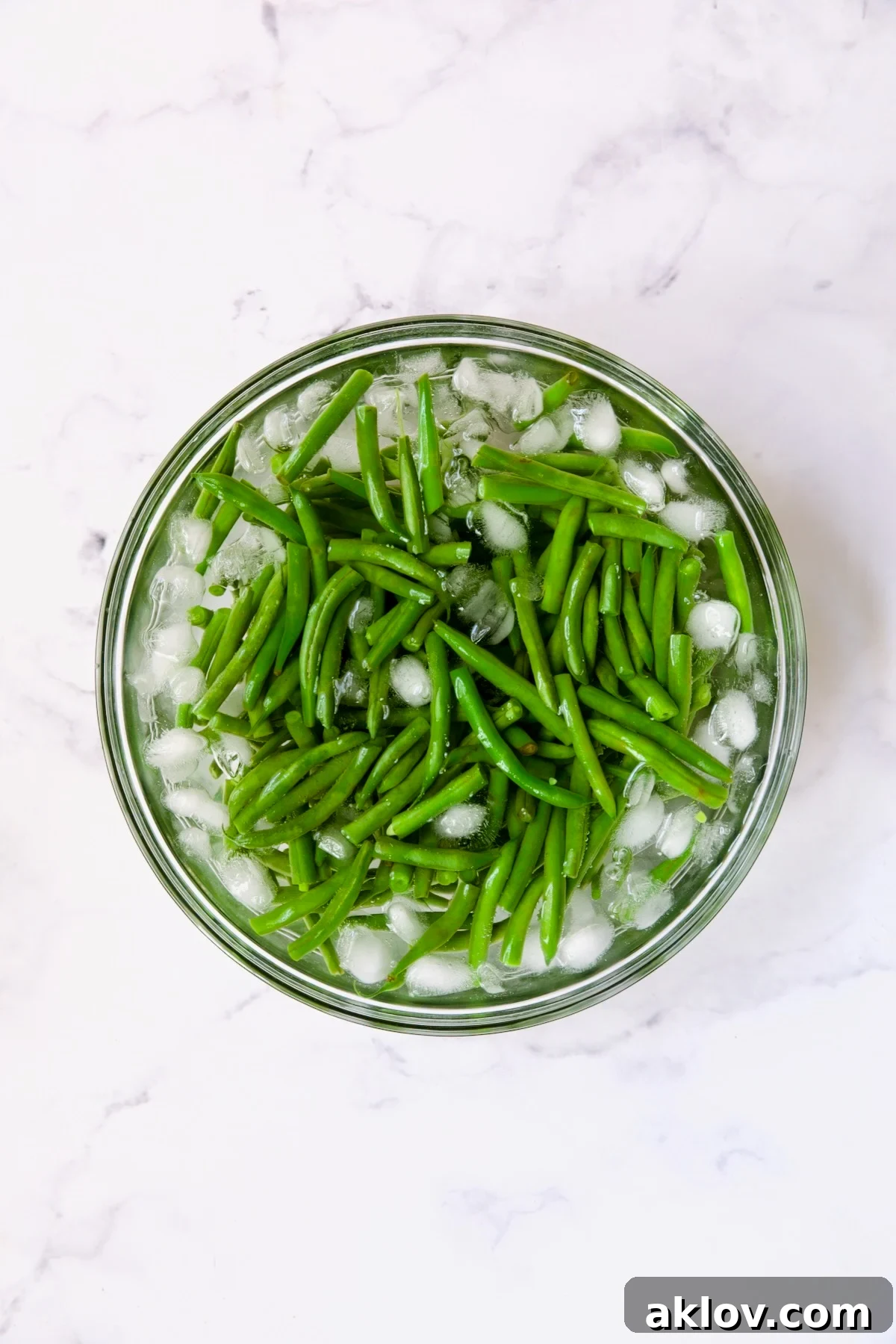 Freshly blanched green beans submerged in a bowl of ice water, maintaining their vibrant green color and crisp texture.