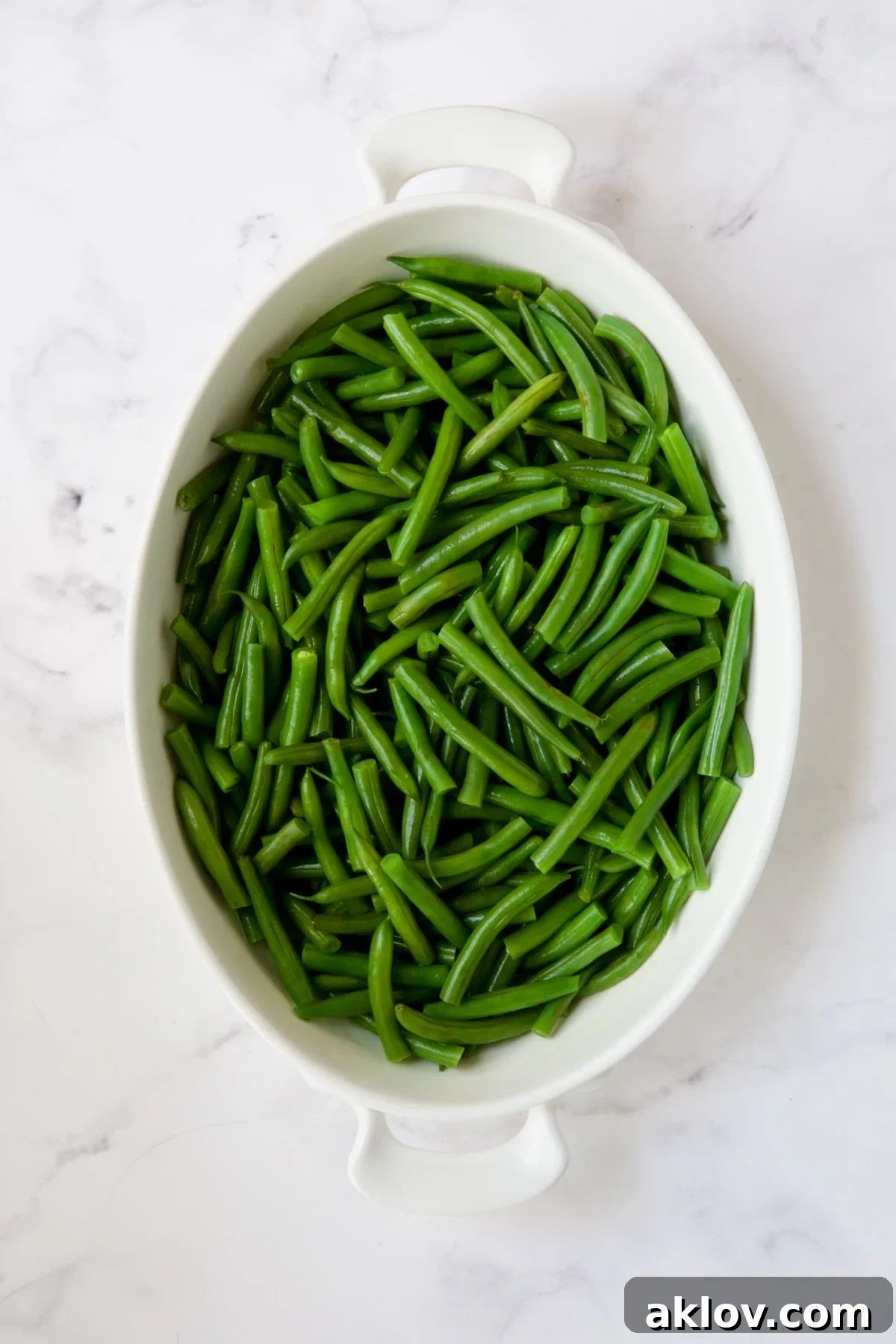 Perfectly blanched green beans neatly arranged in a white oval gratin dish, awaiting the creamy cheese sauce.