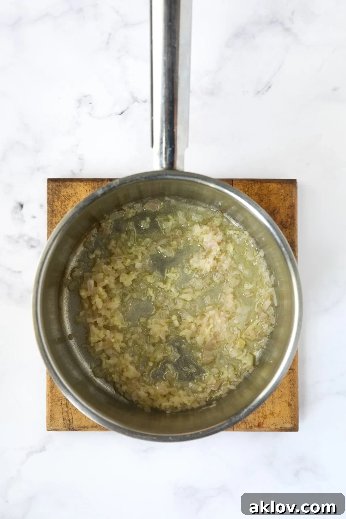 Finely chopped shallots and minced garlic sizzling gently in melted butter within a stainless steel saucepan, releasing their aromatic flavors.