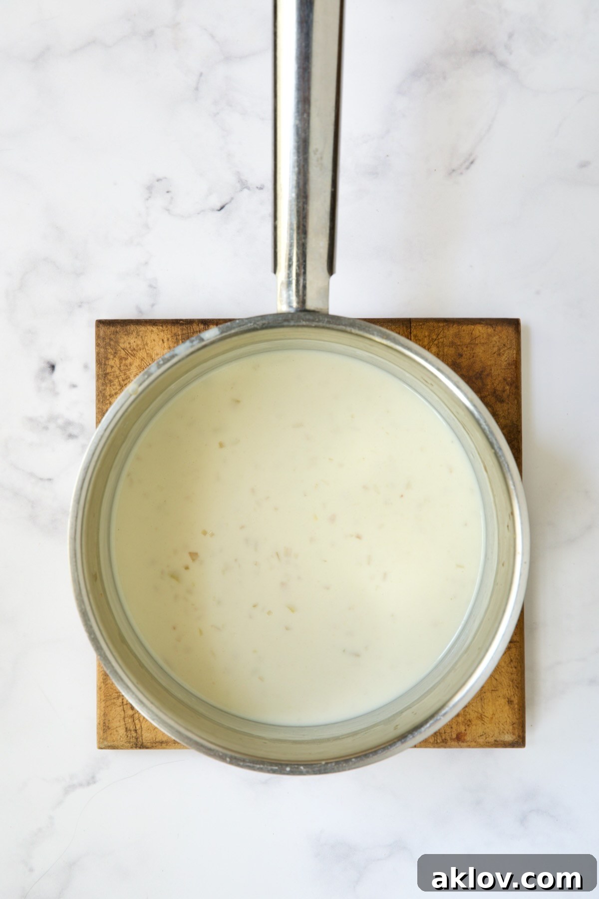 Irresistible Cheesy Green Bean Bake 9 Creamy sauce for green bean casserole simmering in a stainless steel saucepan before cheese is added.
