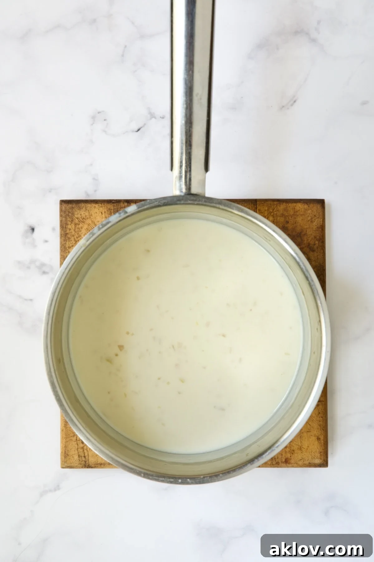 A creamy white sauce simmering in a stainless steel saucepan, perfectly thickened and smooth, ready for the addition of cheese.