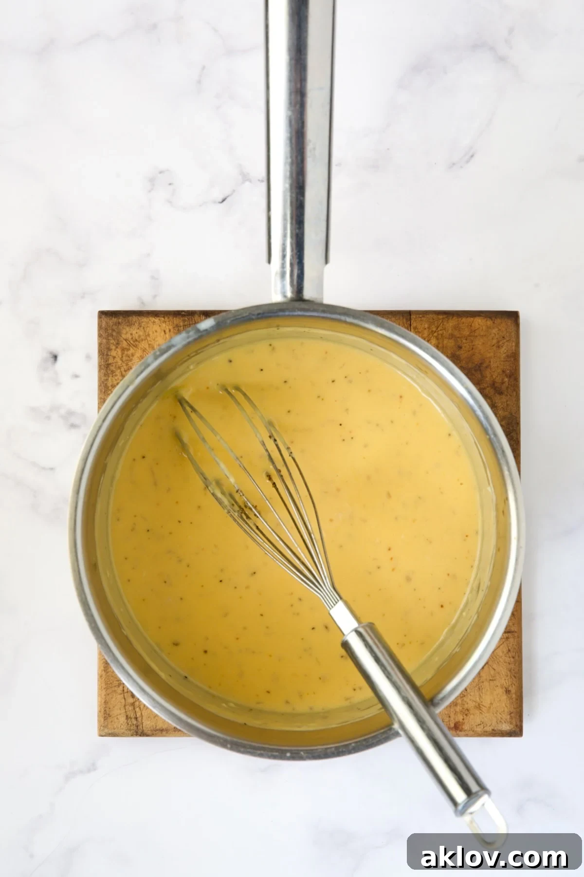 Rich, golden cheese sauce, smooth and perfectly melted, resting in a stainless steel saucepan.