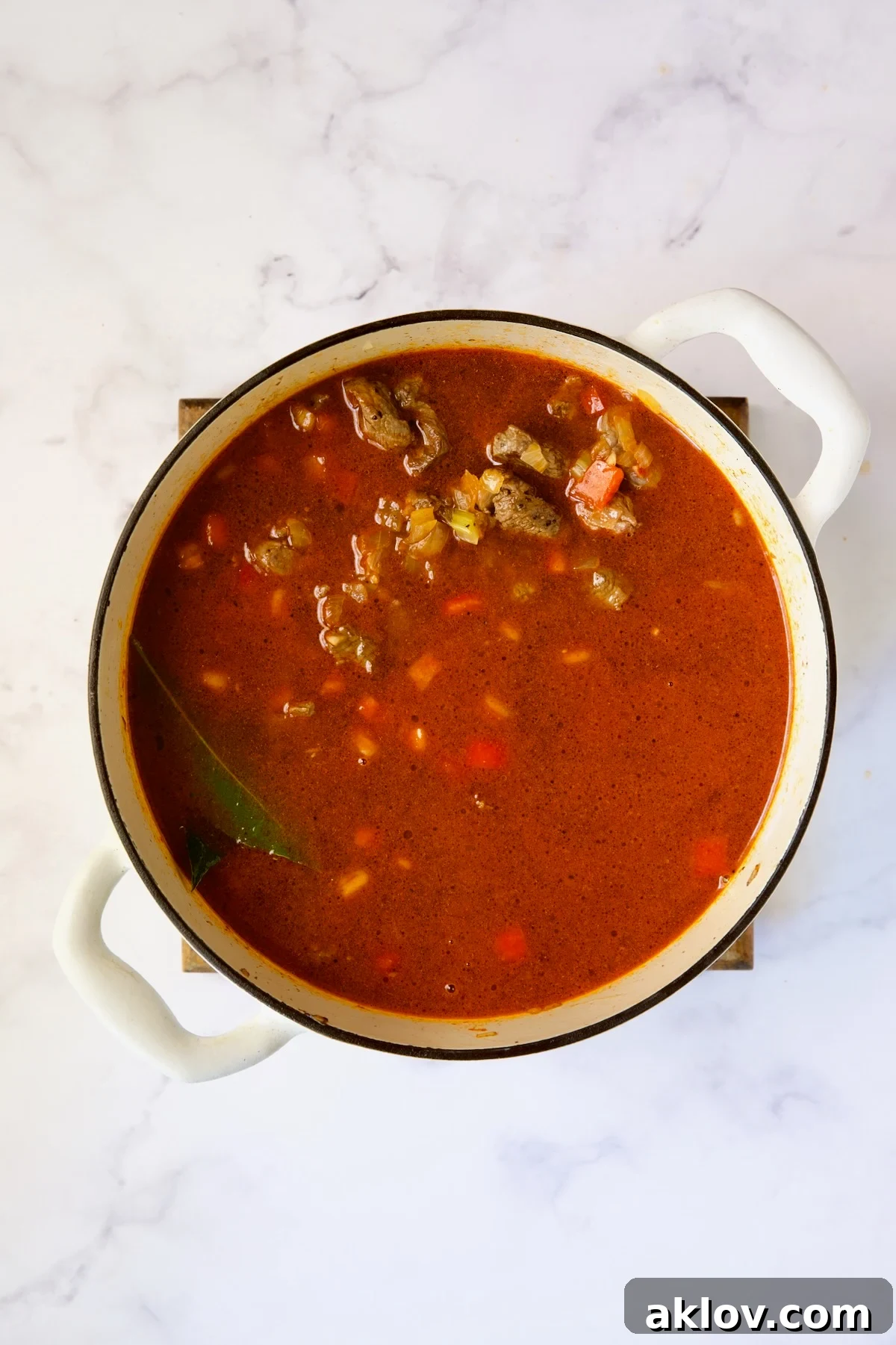 Beef added to goulash in white Dutch oven.