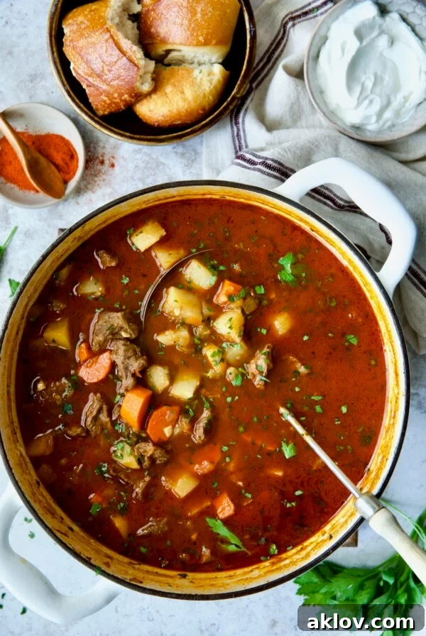 Finished Traditional Hungarian Goulash Soup Recipe in white Dutch oven with bread and sour cream.