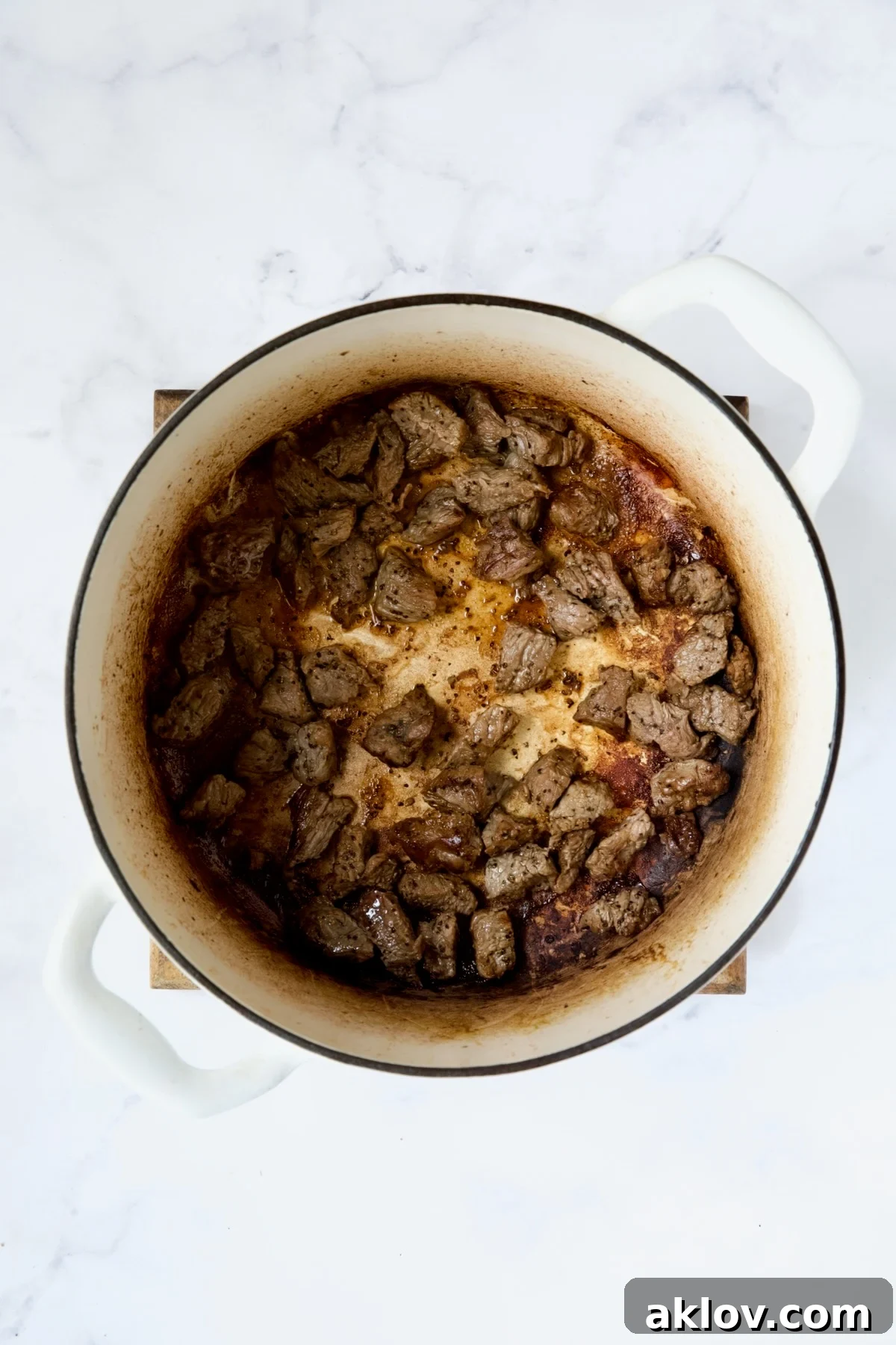 Browned pieces of beef in white Dutch oven.
