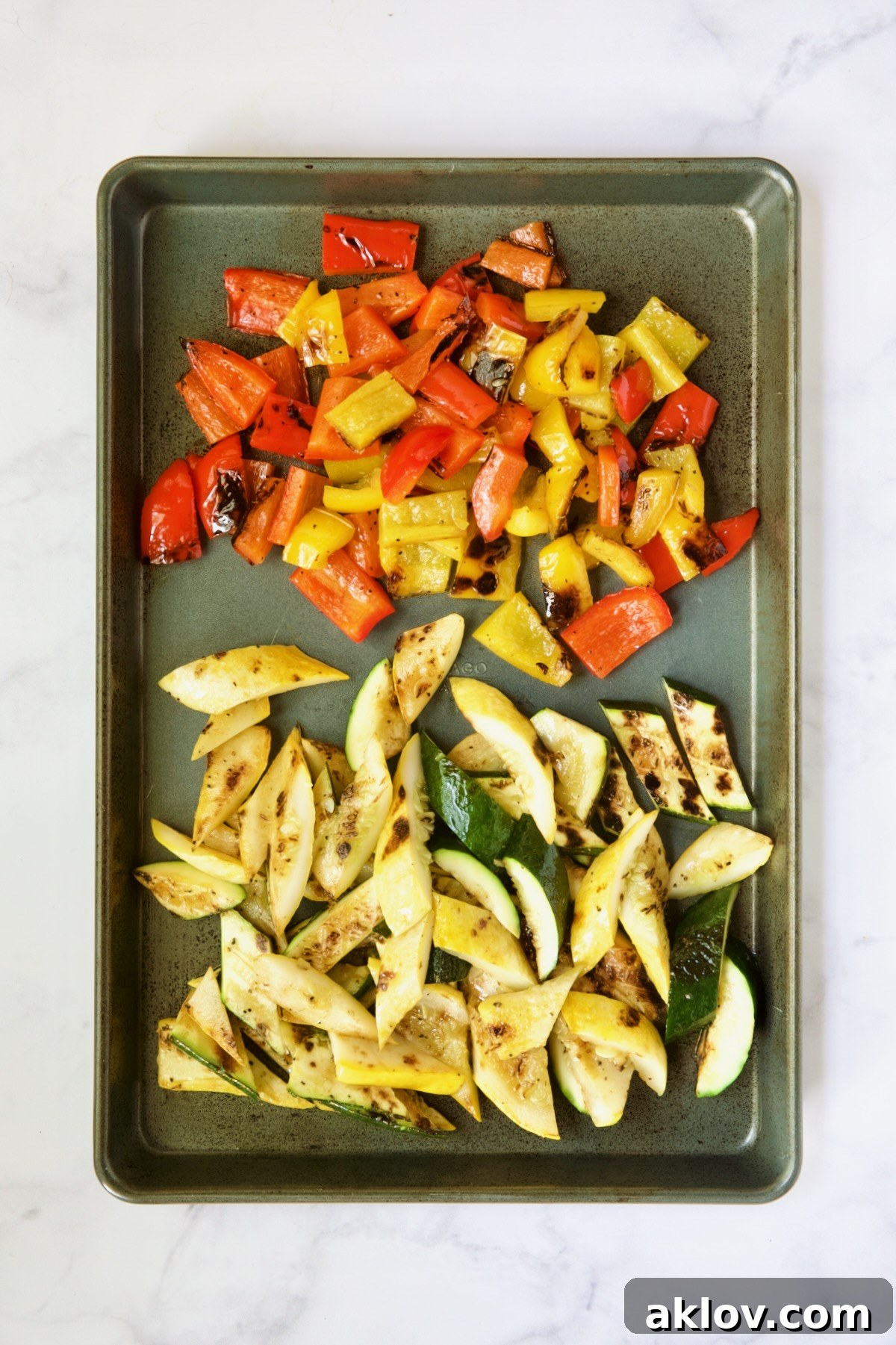 Artfully arranged grilled and sliced zucchini, yellow squash, and bell peppers resting on a rimmed sheet pan, ready to be incorporated into the salad.