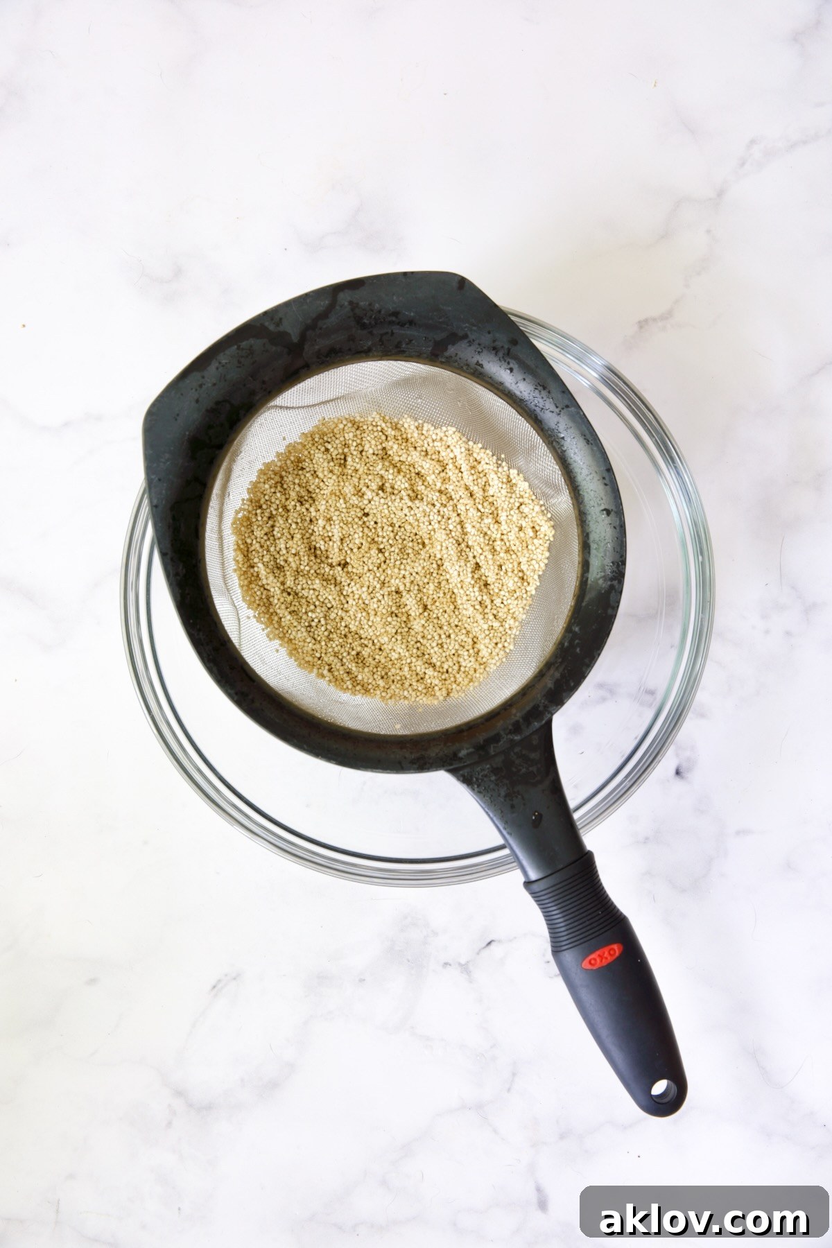 Rinsed quinoa settling in a fine-mesh sieve, positioned over a clear glass bowl, showcasing the thorough rinsing process.
