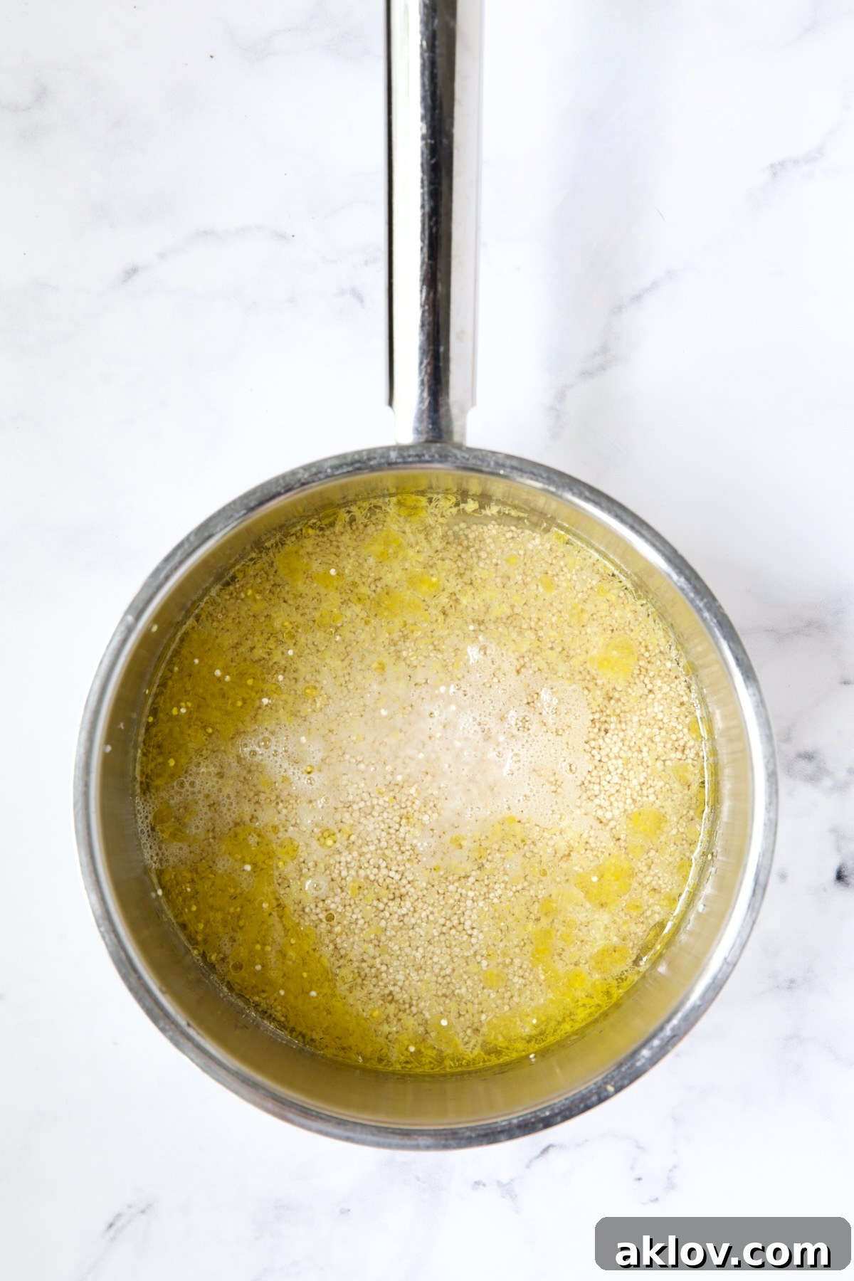 Quinoa, water, and lemon zest simmering together in a stainless steel saucepan, absorbing the aromatic flavors.