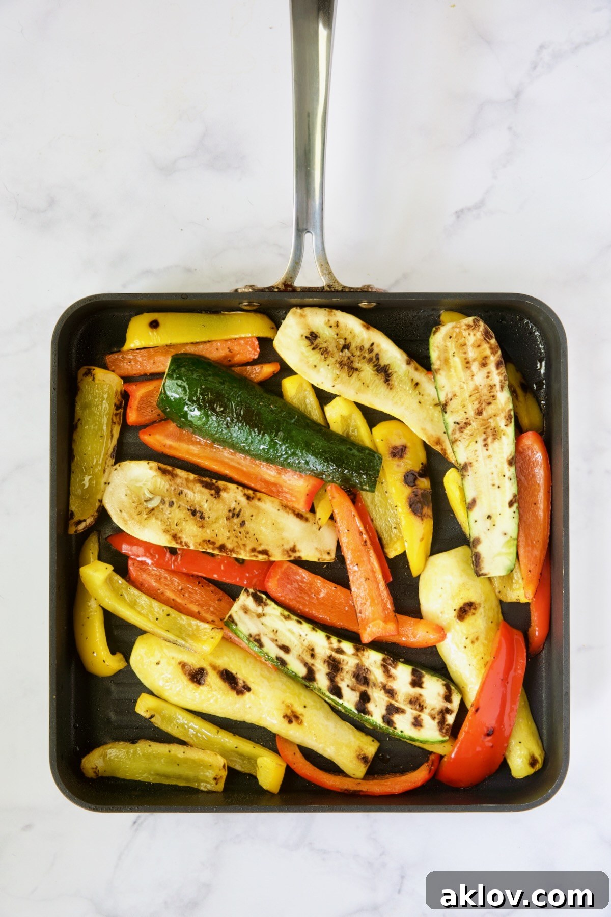 Colorful grilled zucchini, yellow squash, and bell peppers showcasing perfect char marks, arranged on a square grill pan.
