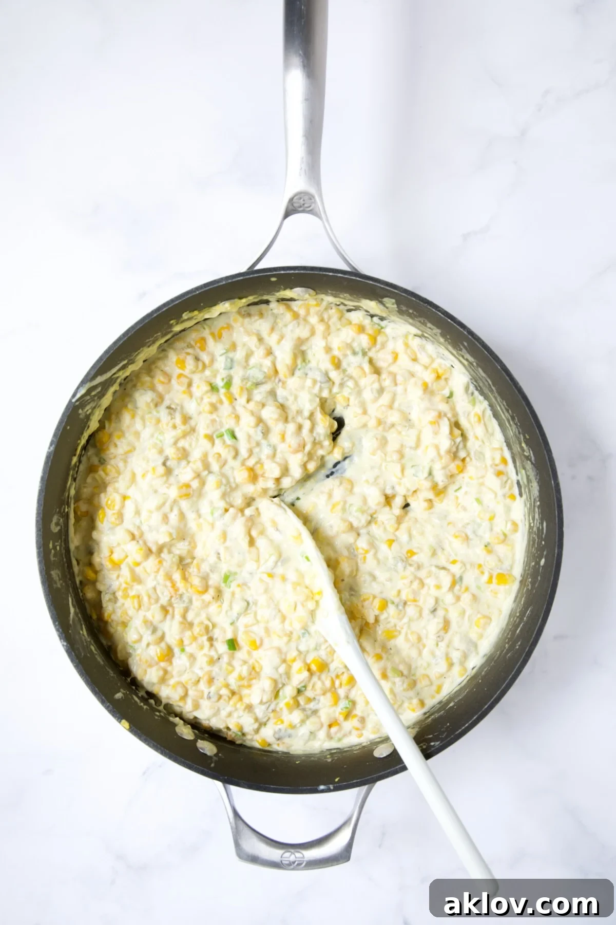 Cream Cheese Corn Casserole with green chiles, now perfectly blended and being stirred with a white spoon.