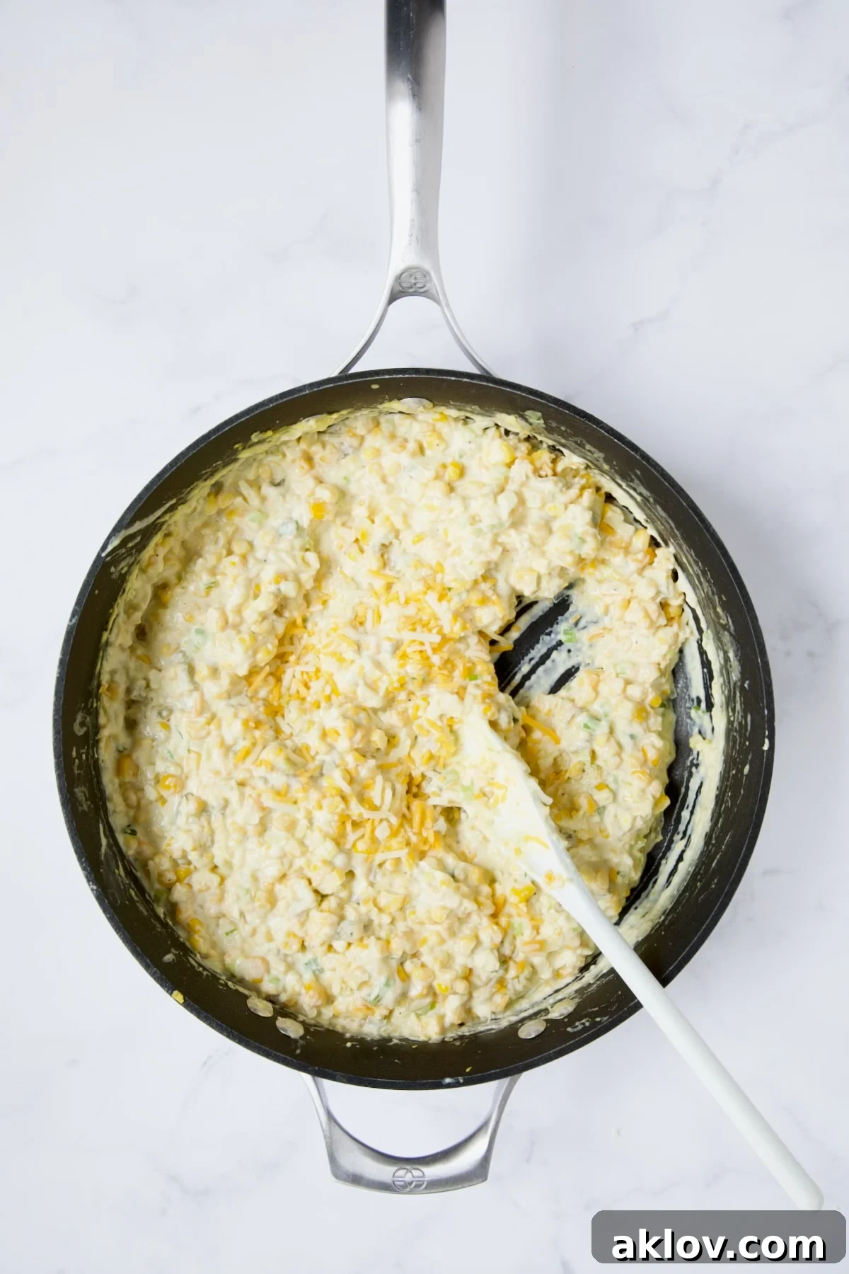 Cream Cheese Corn Casserole in a nonstick skillet, with half of the shredded cheese added and being stirred in.