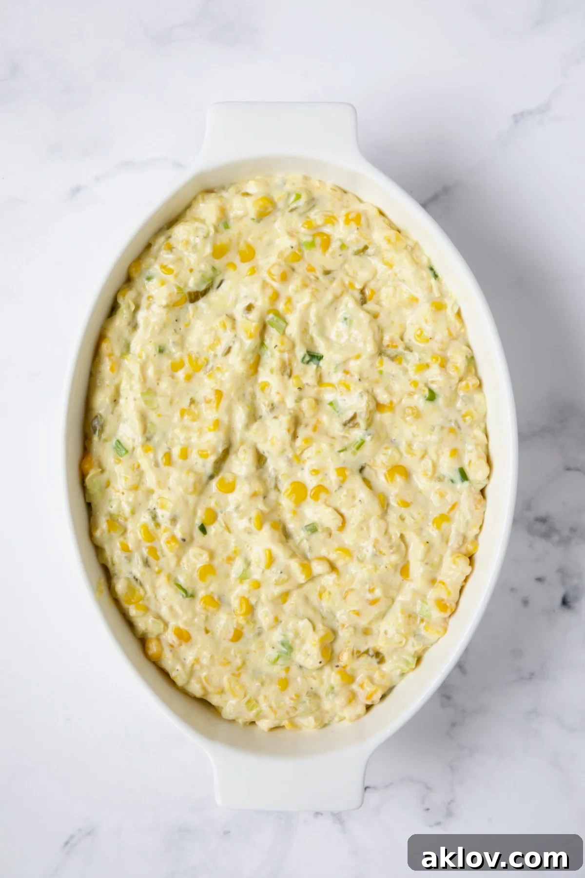 The corn casserole mixture neatly transferred to a baking dish, before the final layer of cheese is added.