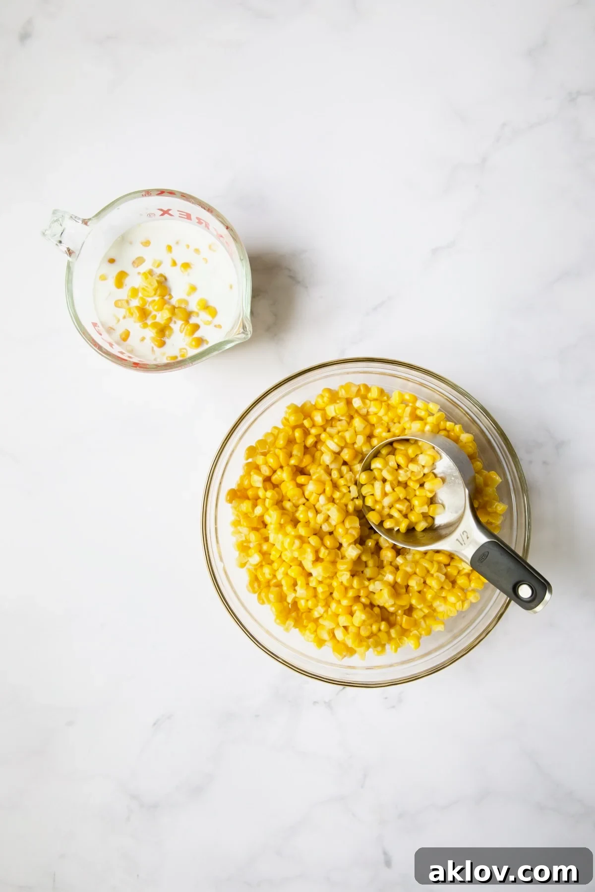 Fresh corn kernels in a glass bowl, with a portion being added to milk in a measuring cup for pureeing.