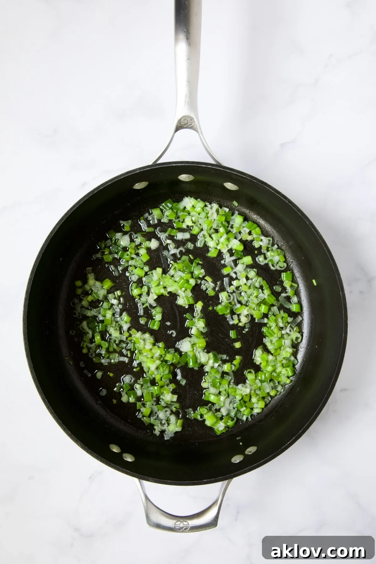 Delicately cooked scallions glistening in melted butter within a nonstick skillet.