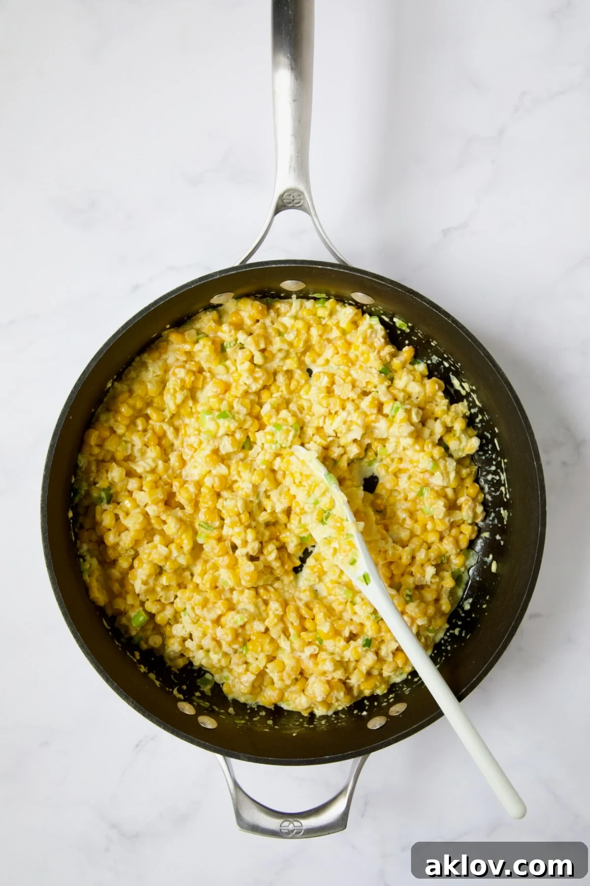 The corn mixture, including both pureed and whole kernels, being stirred in a nonstick skillet with a white spoon.