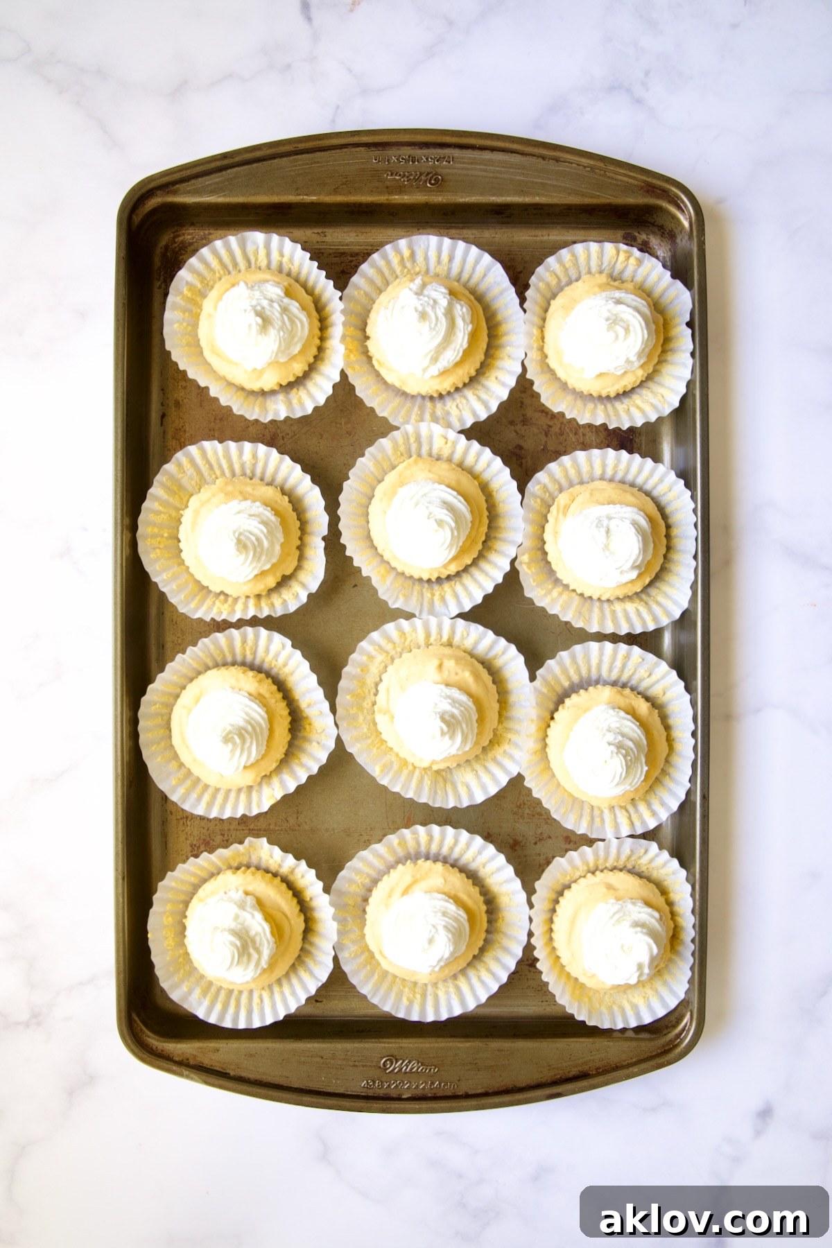 No-Bake Fall Pumpkin Cheesecake Bites 14 Twelve set cheesecakes on white muffin pan liners on a baking sheet, ready for topping.