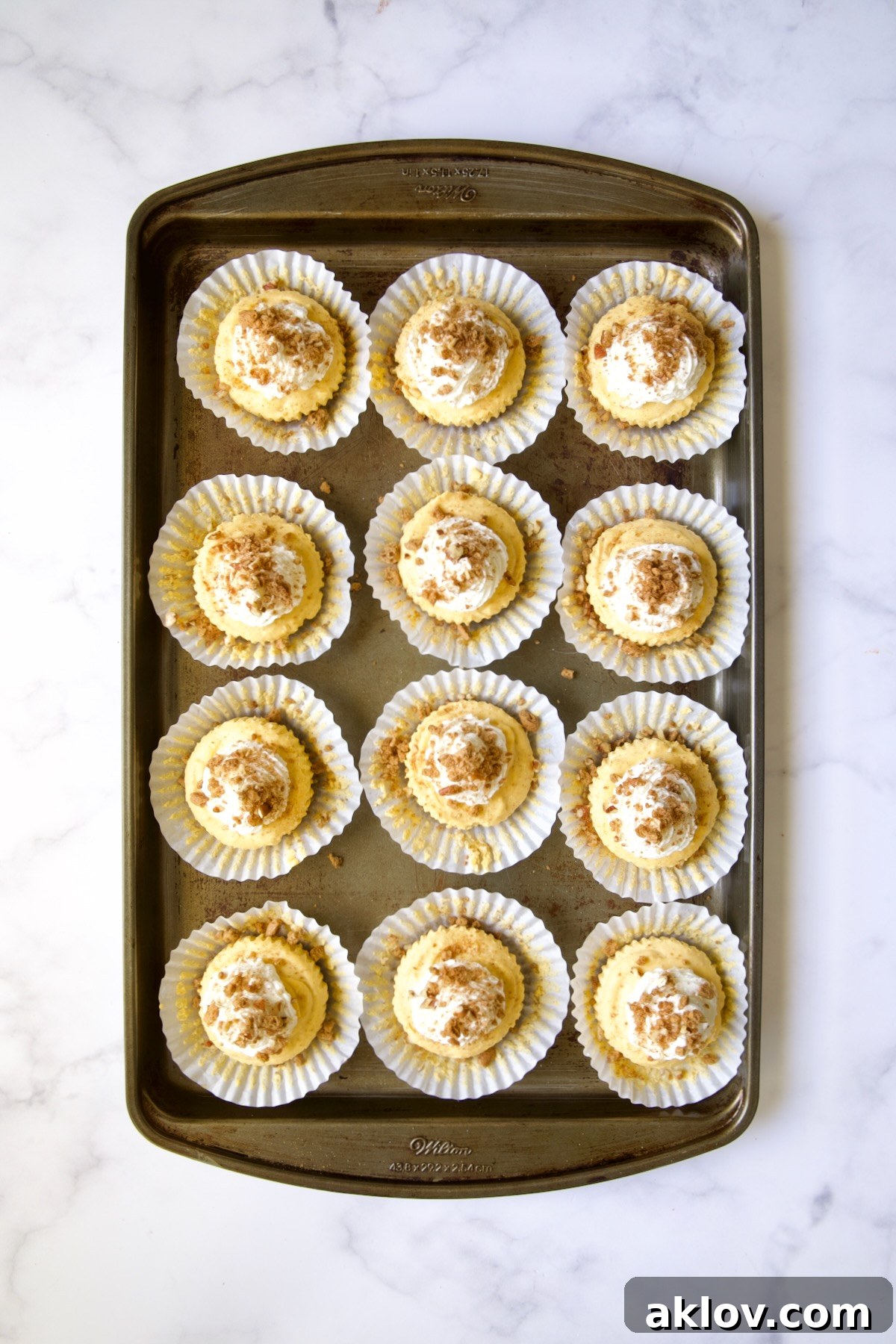 No-Bake Fall Pumpkin Cheesecake Bites 15 Twelve set cheesecakes on white muffin pan liners on a baking sheet with topping sprinkled over.