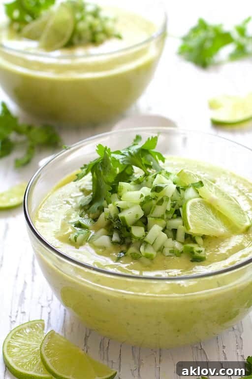 Overhead shot of Cold Thai Cucumber Avocado Soup with Cucumber Relish on a rustic white background, showcasing its vibrant color and fresh toppings.