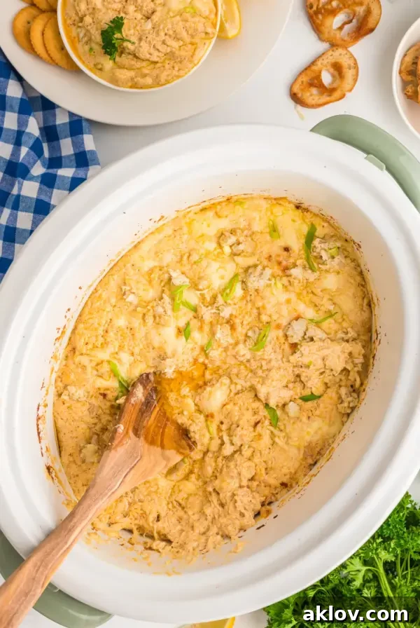 Crab Dip in white slow cooker with wooden spoon stirring it.