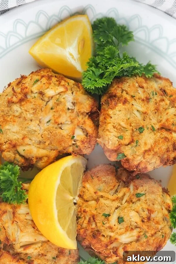 Four Air Fryer Crab Cakes on white plate garnished with parsley and lemons.