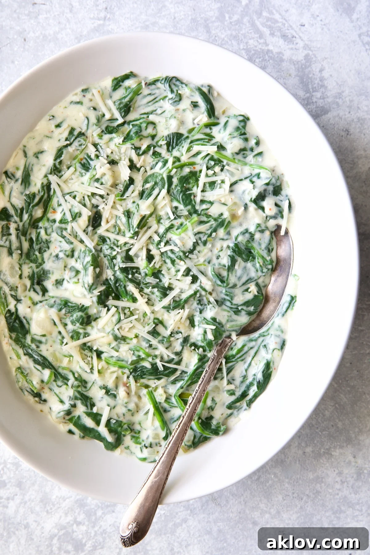 A serving of Steakhouse Creamed Spinach in a white oval bowl with a serving spoon.