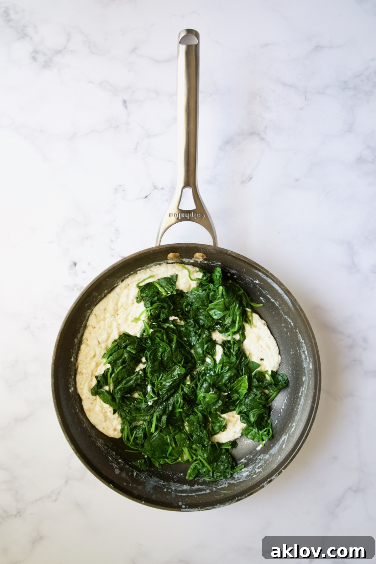 Wilted spinach added to the cheese sauce in a nonstick skillet.