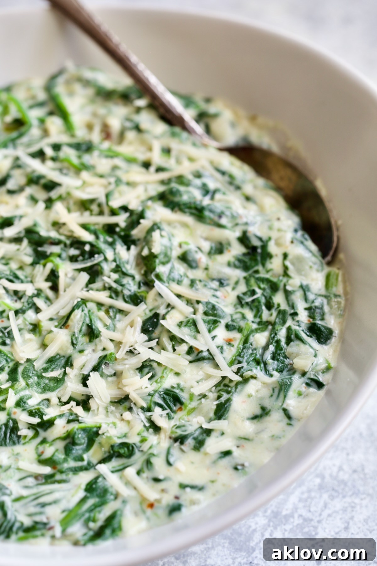 Steakhouse Creamed Spinach in a white oval bowl with a serving spoon, garnished with fresh herbs.