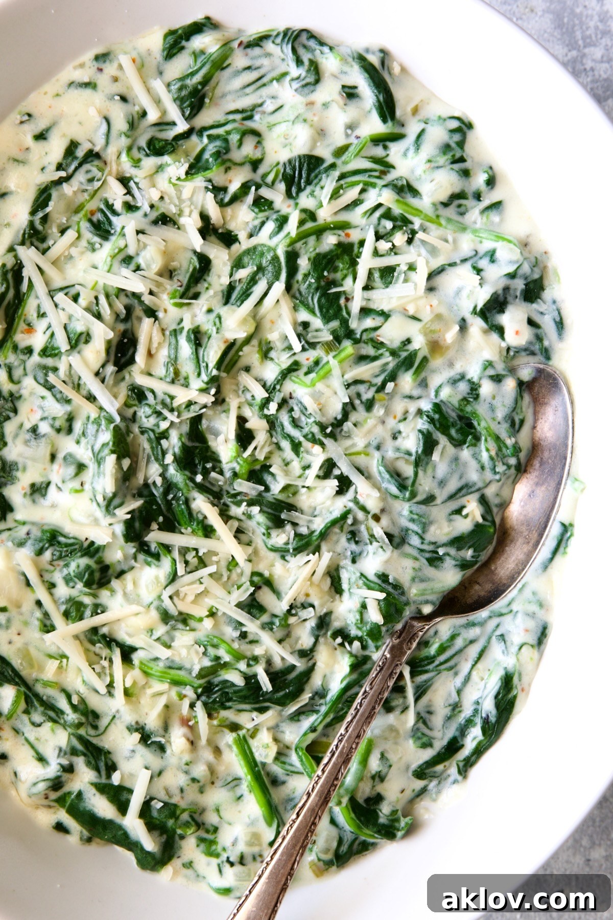 Steakhouse Creamed Spinach in a white oval bowl with a serving spoon, ready to be served.