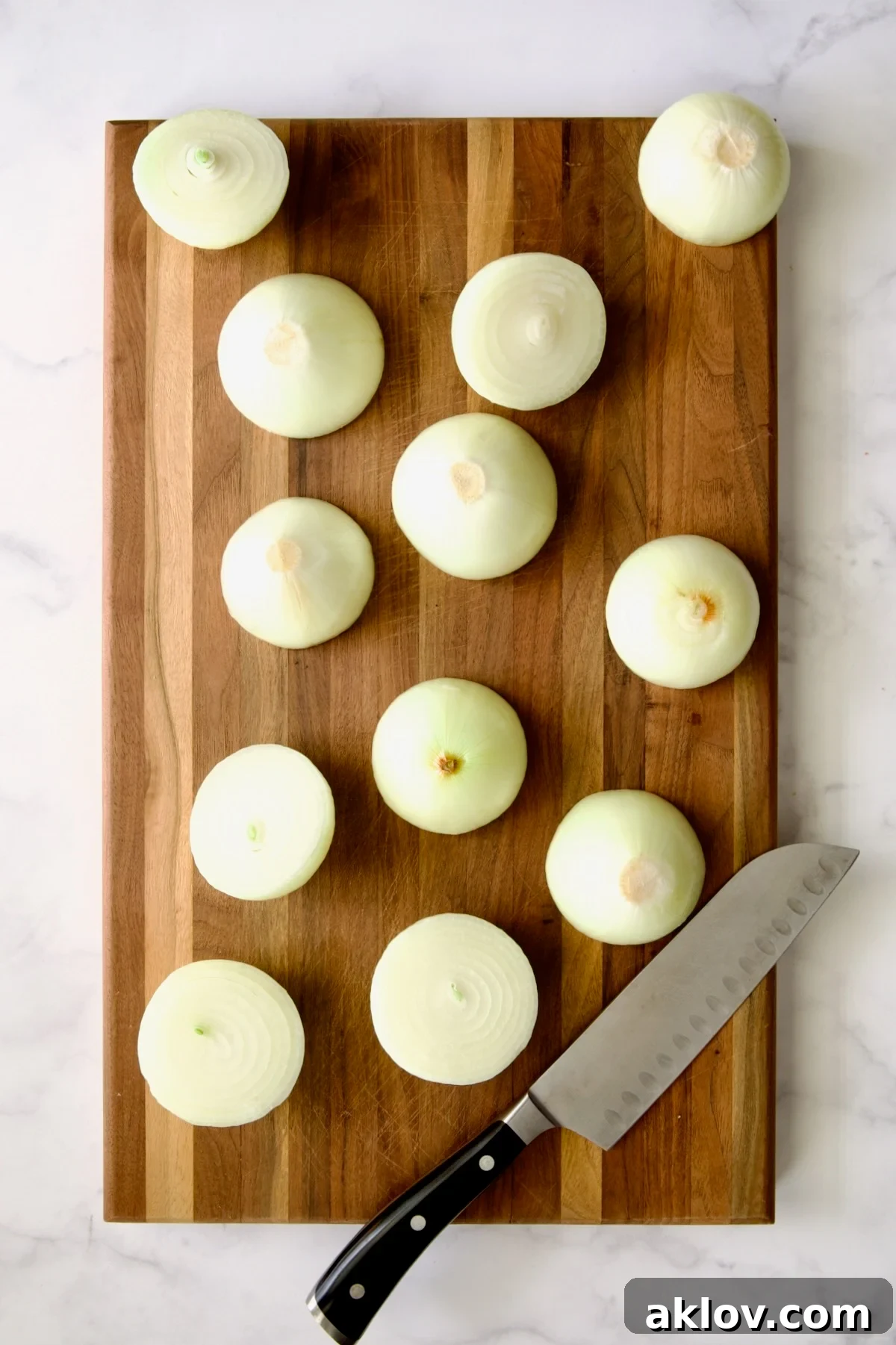 Peeled onions expertly cut in half, revealing their beautiful concentric layers, alongside a chef's knife on a wooden cutting board.