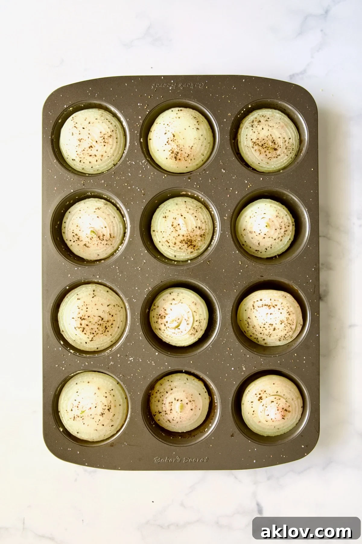 Onion halves resting in a nonstick muffin pan after 20 minutes of initial baking, showing a slight reduction in size and opening of layers.