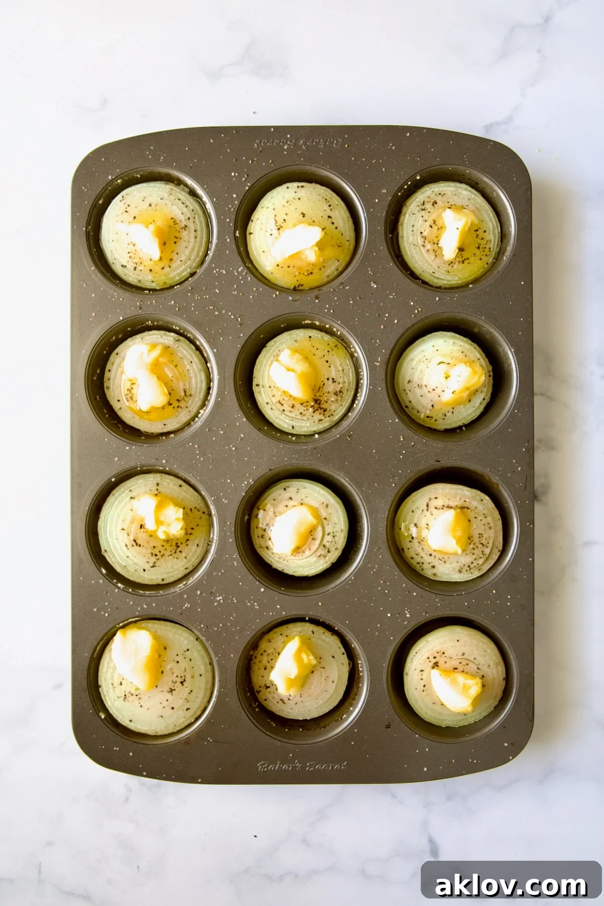 Onion halves in a nonstick muffin pan, glistening with melted ghee applied evenly over their surfaces.