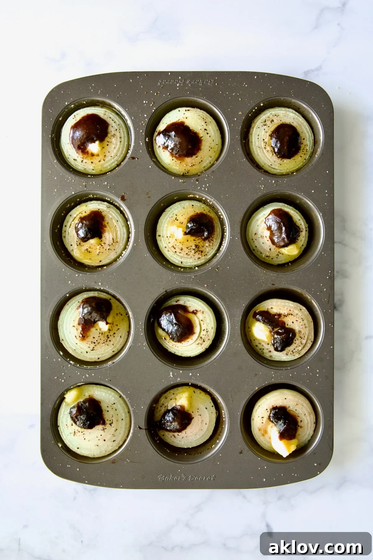 Onion halves in a nonstick muffin pan, now topped with both ghee and beef base concentrate, ready for the next stage of roasting.