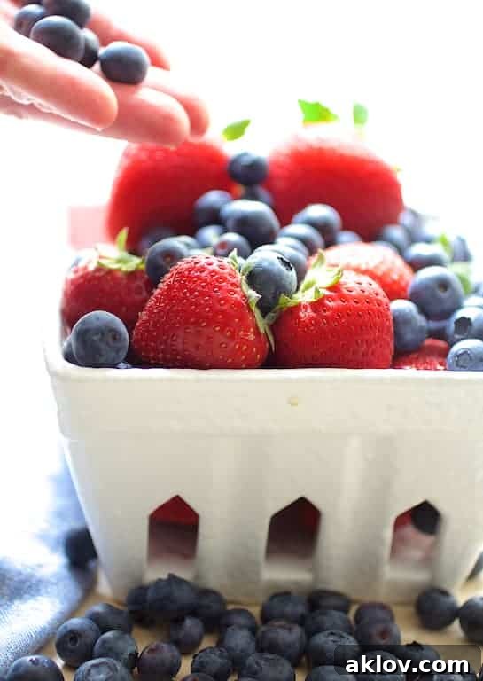 Close-up photo of freshly picked, ripe blueberries and bright red strawberries nestled in a rustic white fruit basket, emphasizing their natural beauty and freshness.