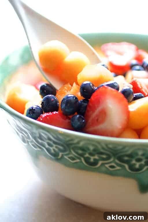 Overhead shot of fresh, colorful fruit salad being gently stirred in a spacious white bowl with a matching spoon, showcasing the mix of berries and melon.