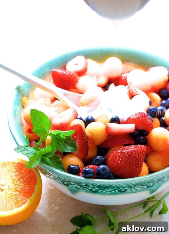 Close-up action shot of the smooth, creamy Orange Vanilla Yogurt Dressing being poured generously over the vibrant fruit salad, highlighting its rich texture and color.