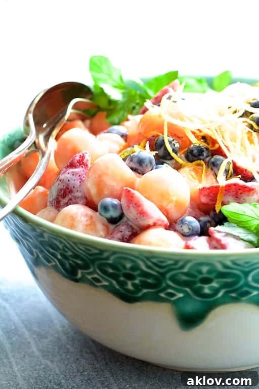 Artful close-up of the Summer Fruit Salad with Orange Vanilla Yogurt Dressing served in a chic green and white decorative bowl, showing off the vibrant colors and appealing texture of the dressed fruit.