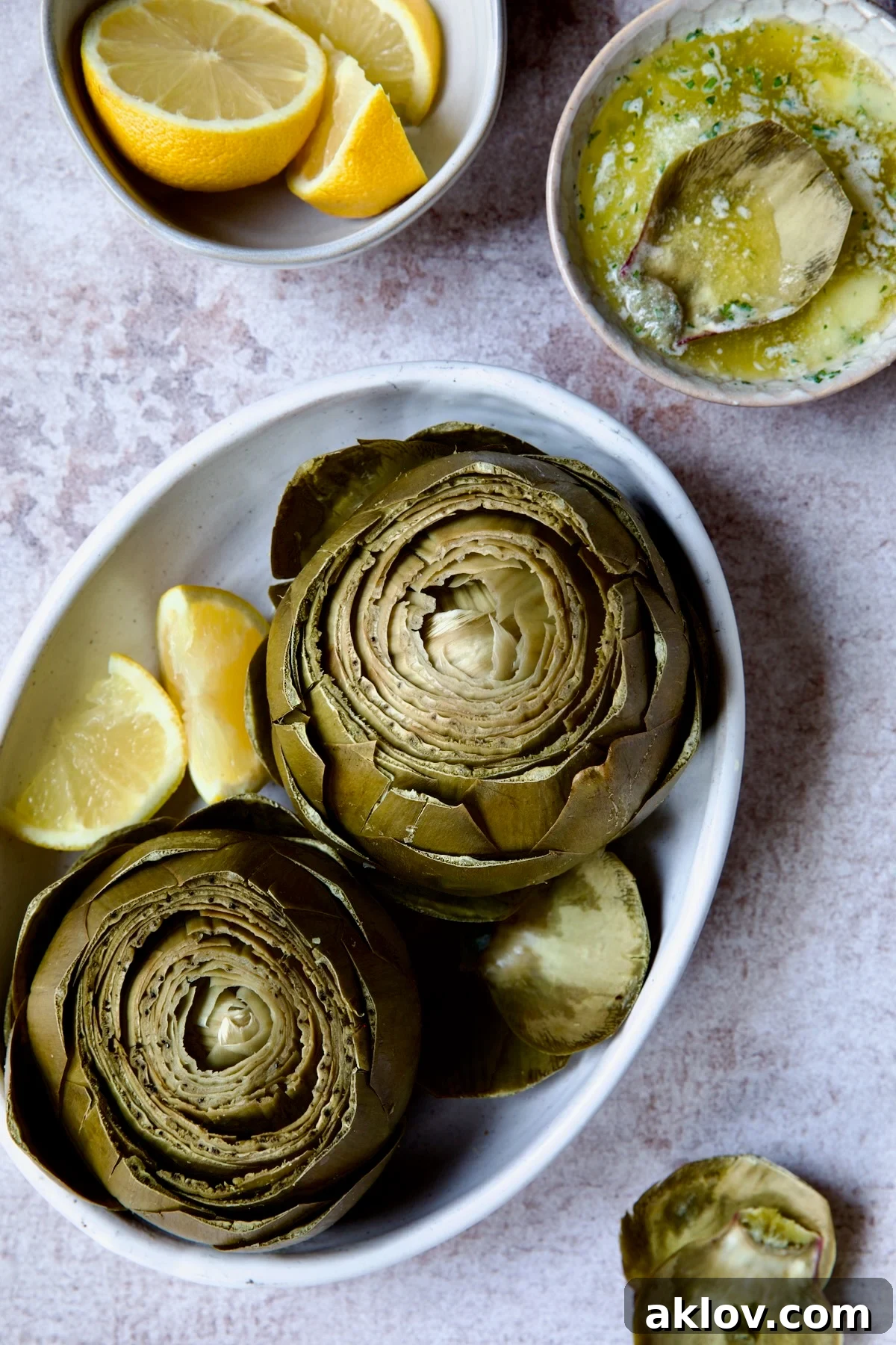Perfectly steamed Instant Pot Artichokes with a side of creamy garlic butter and fresh lemon wedges, arranged in a white oval serving bowl.