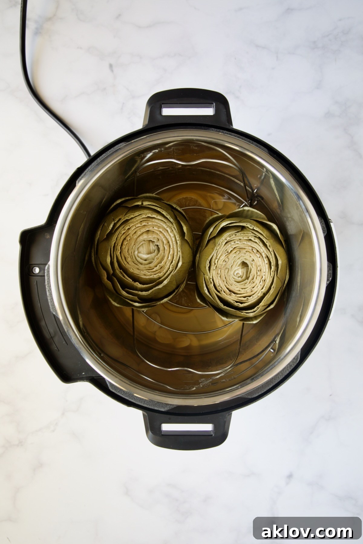 Two perfectly steamed artichokes resting in the Instant Pot after cooking, appearing tender and ready to serve.