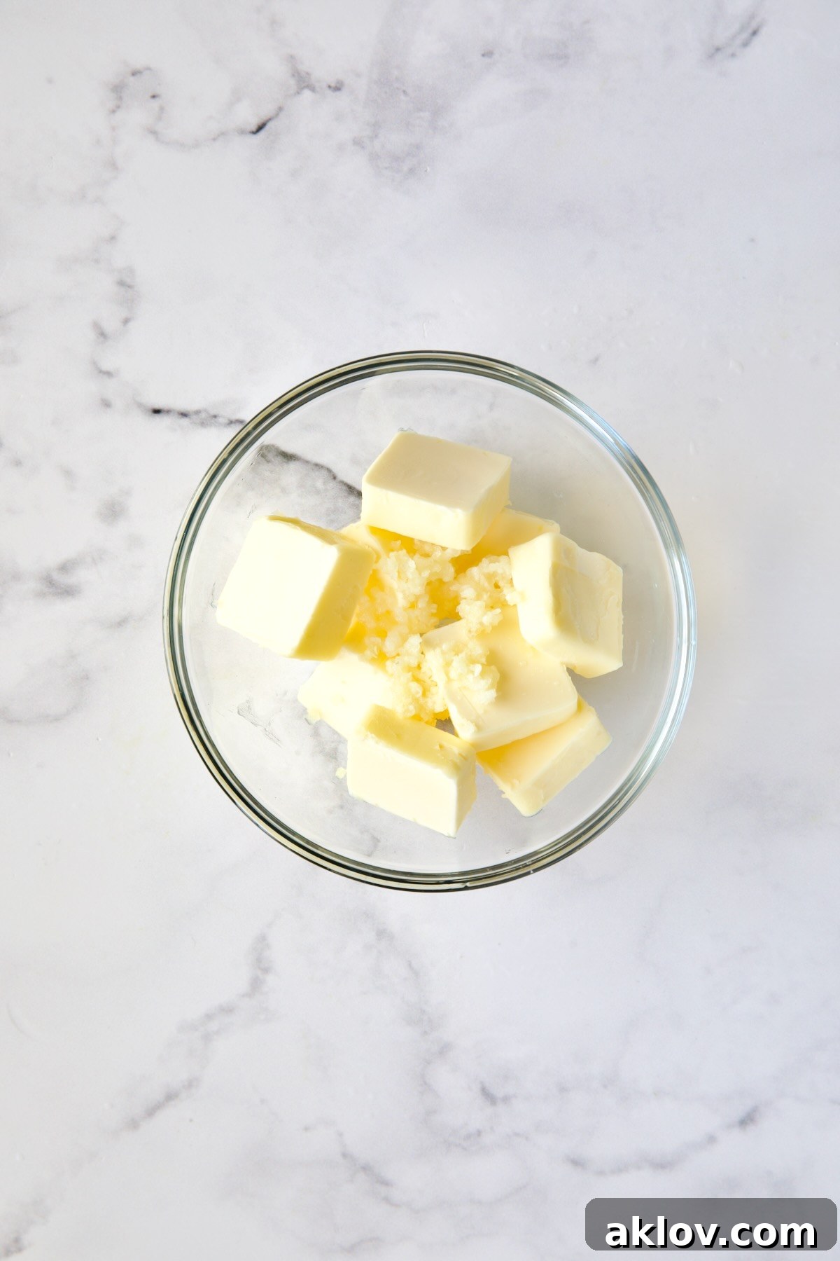 Slices of butter and finely minced garlic cloves in a clear glass bowl, prepped for microwave melting.