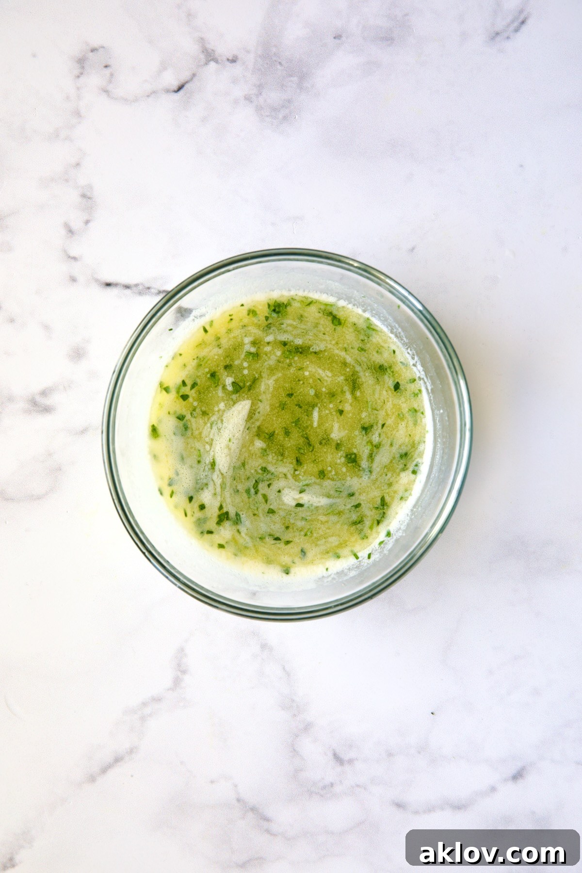 Melted garlic butter in a glass bowl, now with fresh chopped parsley stirred in, ready for serving.