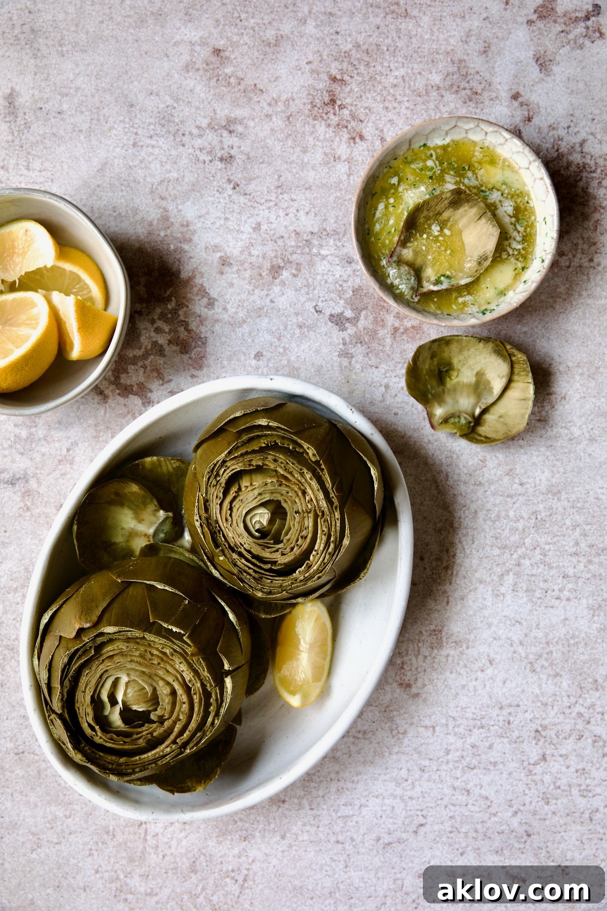 A beautifully presented serving of Instant Pot Artichokes in a white oval bowl, accompanied by a small dish of garlic butter and fresh lemon wedges, ready to be enjoyed.