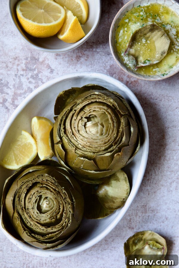 Instant Pot Artichokes with Garlic Butter, beautifully presented in a white oval serving bowl with lemon wedges, ready to be enjoyed.